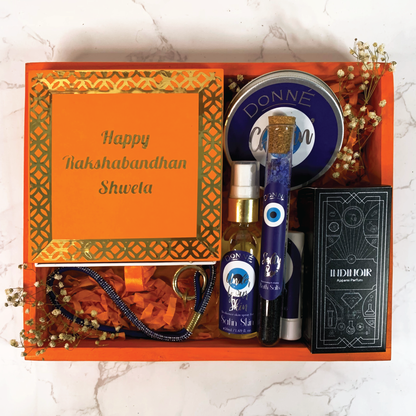 Assortment of products in a vibrant orange festive hamper with mithai scented candles, dazzling phone slings, moisturising body spray, portable solid perfume, lightweight facial moisturising cold cream, perfume and bath salts