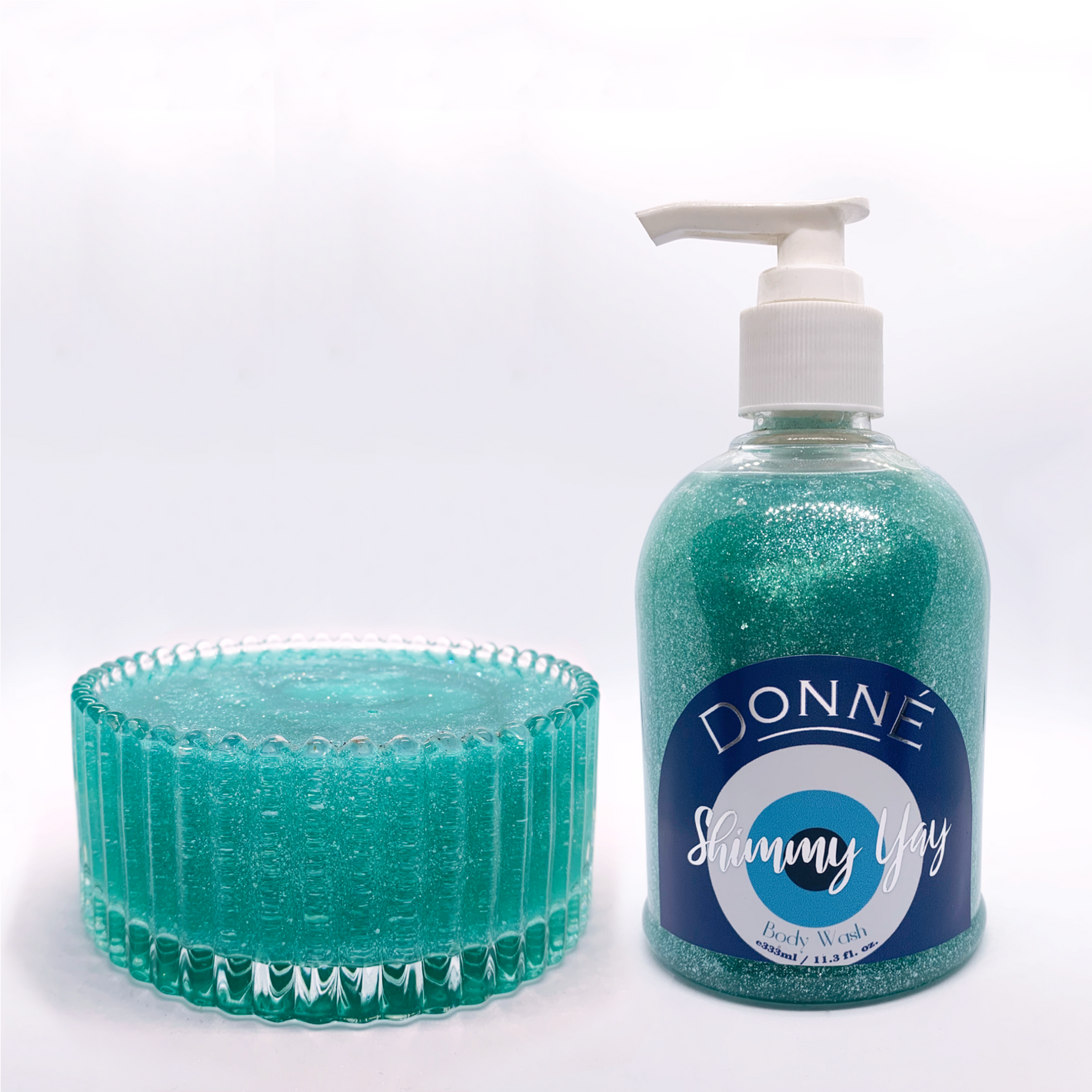 Round dome shaped bottle with turquoise blue shimmering body wash with evil eye label with metallic accents and pump and a glass bowl with a pool for a texture swatch